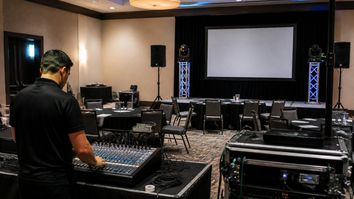 A small corporate event setup in a hotel conference room, with a compact sound system, LED stage lights on stands, and a projection screen showing a presentation slide. ### Sound, Lighting, and Video at Small Scale **Sound** is the system most likely to be undersized. A single wireless handheld mic works for a keynote, but a four-speaker panel needs four channels and someone mixing them live. **Lighting** does two jobs: it makes the stage readable on camera and separates the presenter from the background. **Video** usually means a projection screen for slides, a camera feed for overflow rooms, or a live stream for remote attendees. :::tip Ask your venue for a floor plan with power outlet locations before you spec any equipment. We have seen more setups delayed by a missing outlet near the stage than by any equipment failure. ::: ## Your Corporate Event Production Checklist A corporate event production checklist should cover the timeline from booking to breakdown, not just the day itself. The most common mistake is treating production as a last-week task: vendors book out, equipment gets reserved, and rush fees add up. Work backward from the event date and assign an owner to every step. ### The Production Timeline, Worked Backward **Eight to twelve weeks out, Scope and book.** Confirm the venue, date, and room dimensions. **Four to six weeks out, Lock the plan.** Select the vendor and sign the scope of work. **One week out, Rehearse and confirm.** Schedule a technical rehearsal in the actual room. **Event day, Execute and adapt.** Arrive for the setup window with time to spare. **After the event, Capture and review.** Collect the recording and any attendance or engagement data. ### The Steps Teams Skip Most Often The technical rehearsal is the step teams skip most often. Walking the room with your presenters, testing every mic, and running the first five minutes of the program catches problems while there is still time to fix it. The second most-skipped step is confirming venue AV terms in writing. Many contracts list in-house equipment as an add-on, and some venues require you to use their technician at an hourly rate. :::warning Do not assume the venue's in-house AV is included in your rental fee. Confirm it in writing before you sign, and confirm whether you are permitted to bring your own equipment and crew. ::: ### Assign an Owner to Every Line A checklist without owners is a wish list. For each step, name one person responsible and one backup. On small teams, the same person often holds several roles, which is exactly why the timeline matters: it spreads the work across weeks instead of concentrating it into the final days. :::takeaway Work backward from the event date, assign an owner to every step, and treat the technical rehearsal as non-negotiable. That sequence is what separates a smooth program from a morning of improvisation. ::: ## How to Write an Event Production Brief That Gets Results An event production brief is a short document that tells your vendor what the event needs to accomplish, not just what equipment to bring. A good brief fits on one page. We ask every client for four things: the event goal, the audience, the run of show, and the venue details. That is enough to build an accurate quote and flag problems early. ### What to Put in the Brief (and What to Leave Out) Include the event type and purpose, the number of attendees, the room layout, the schedule, the list of speakers, and any recording or streaming requirements. Leave out equipment brand preferences unless you have a specific technical reason. Telling a vendor which mixer to bring limits their ability to solve your actual problem. Describe the outcome you want, and let the production team match the gear. :::warning Do not assume the venue's in-house AV is included in your rental fee. Many contracts list it as an add-on, and some venues require you to use their technician at an hourly rate. Confirm this in writing before you sign. ::: ## Production Services for Small Corporate Events: Budget and Vendor Selection [Production services for small corporate events