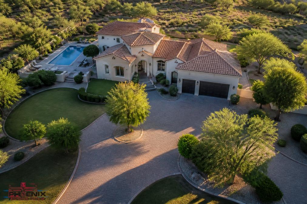 Aerial perspective of upscale residential property with manicured landscape captured from drone, showing smooth, stable footage with sharp detail of roofline, driveway, and architectural features in golden afternoon light