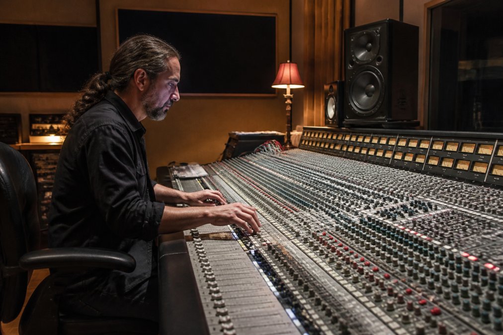 Mastering engineer adjusting faders on a mixing console for film post-production in a professional studio