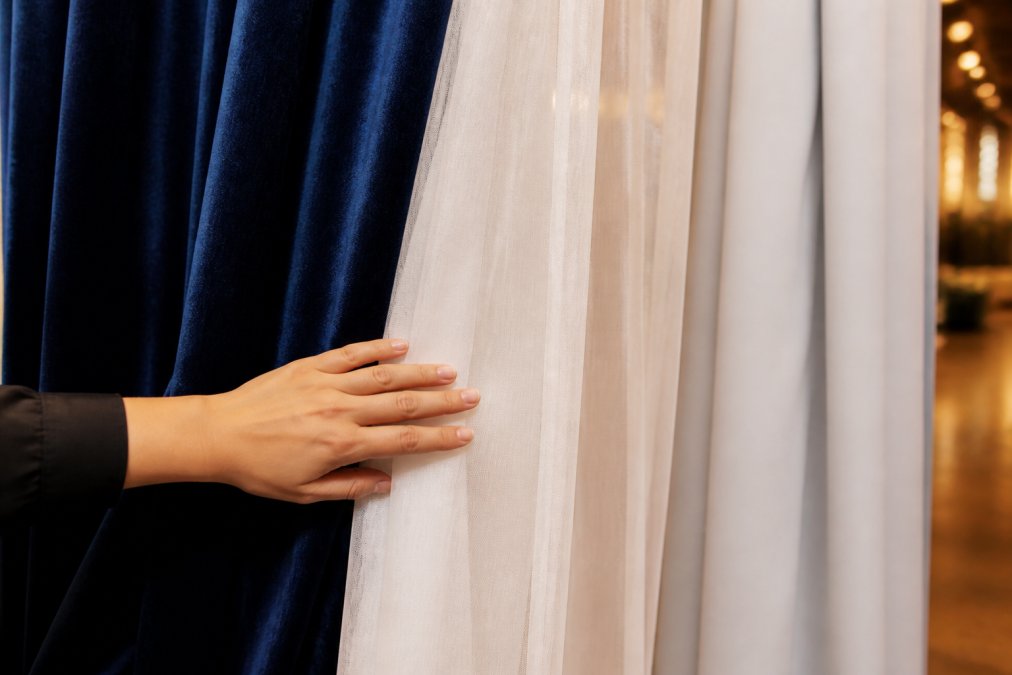 Close-up of a hand running across three hanging drape fabric swatches in velour, sheer, and poly-premier, soft ballroom lighting