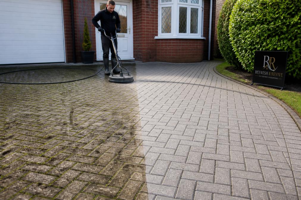 A residential block paving driveway in two halves: left side showing heavy moss growth, dark algae staining, and visible grime buildup on the surface; right side showing the same driveway restored to a clean, brilliant grey tone with clear joint lines, photographed in natural daylight
