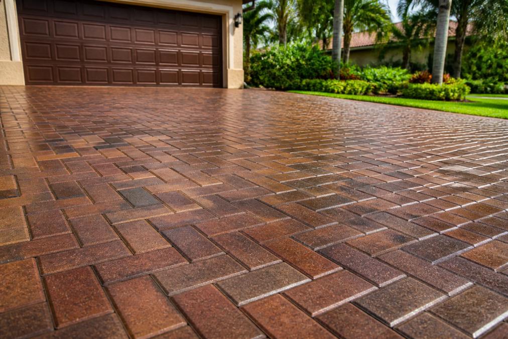 Close-up of freshly sealed brick pavers on a residential driveway glistening under afternoon Florida sunlight, showing a rich, even finish with no staining or discoloration, surrounded by green landscaping