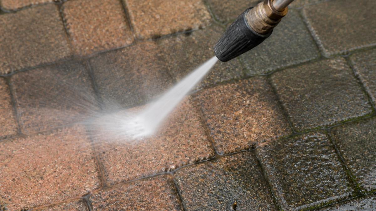 Close-up of a pressure washer nozzle positioned near block paving surface, showing the concentrated force of water spray hitting the blocks at close range