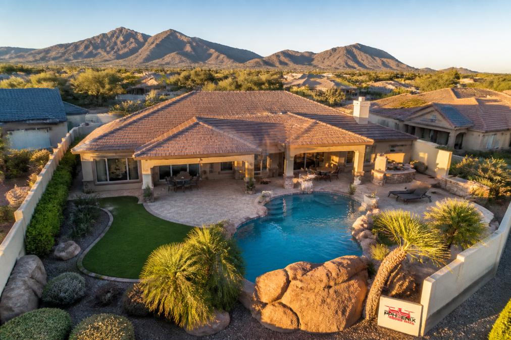 Aerial view of a residential property with sparkling pool, manicured landscaping, and mountain backdrop captured from a drone at golden hour, showing clear detail and professional composition