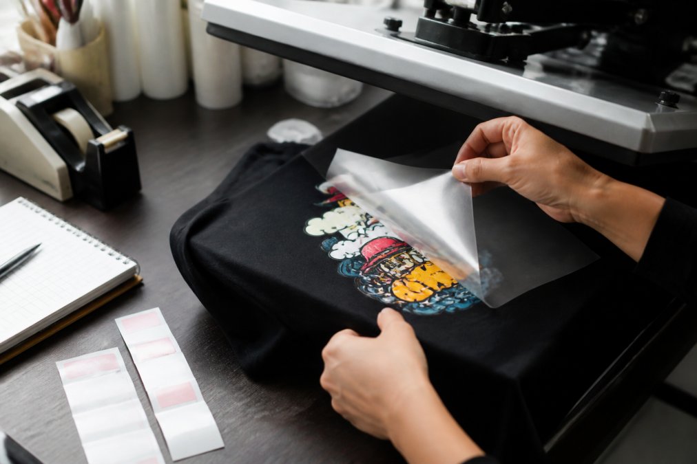 Hands peeling a DTF transfer from a cotton shirt to check dtf transfer quality before production.