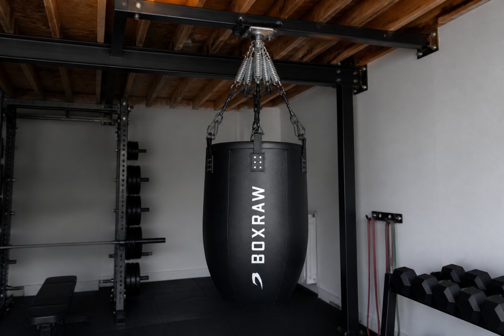 Installed heavy bag with swivel hanger and commercial-grade spring system in home gym, showing complete suspension setup with proper clearance around the bag and isolation pads under mounting structure