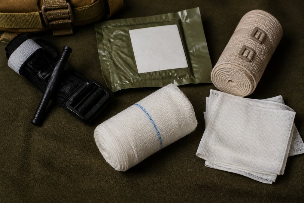 Close-up of professional wilderness trauma supplies laid out on a neutral surface, including a tourniquet, hemostatic dressing, pressure bandage, and sterile gauze organized by type