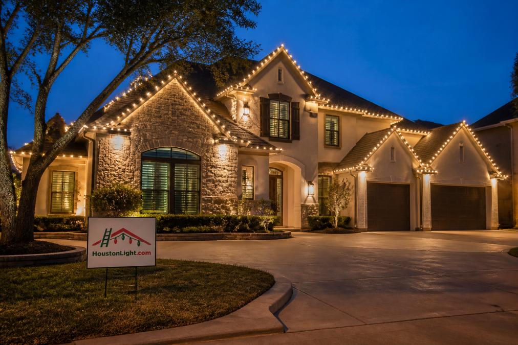 Completed residential holiday lighting display at dusk showing elegant, professionally installed lights outlining roofline and architectural features with warm glow illuminating home