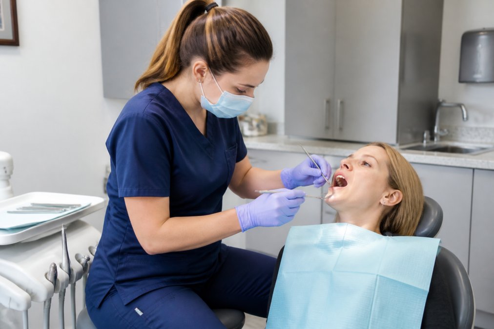 Dental hygienist wearing well-fitted professional scrubs with visible utility pockets actively working at a patient chair, demonstrating freedom of movement and comfort during clinical work with instruments and tools nearby