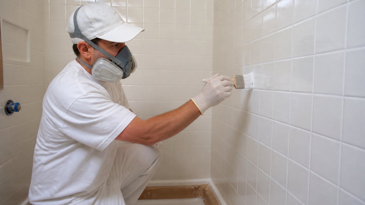Professional applying epoxy coating to shower tile with precision brush, creating glossy finish in well-lit bathroom workspace