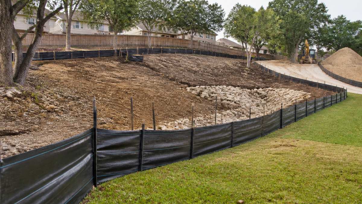 Construction site in San Antonio with silt fencing and sediment barriers installed along disturbed slopes, protecting landscaped areas during active soil work, showing proper erosion control infrastructure in place