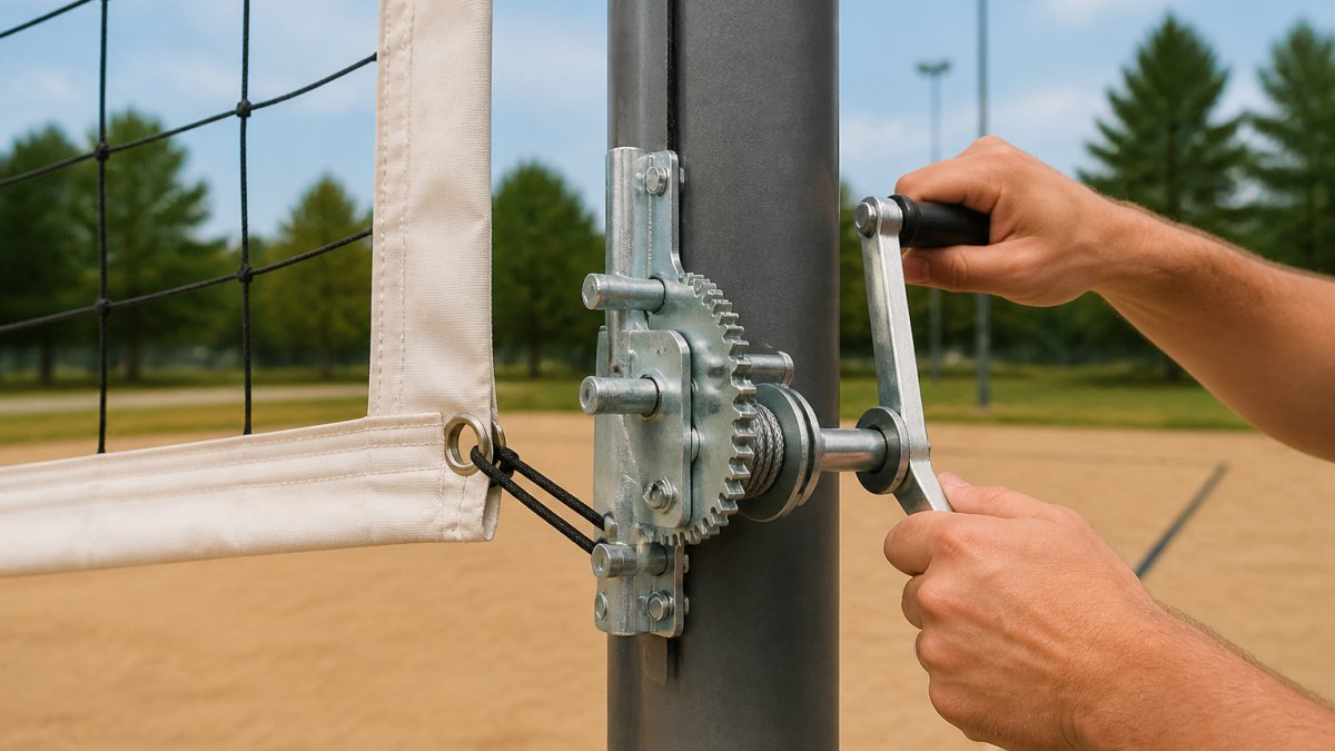 Close-up of a wormgear crank tensioner system on a volleyball net post, showing the mechanical components and adjustment mechanism with hands demonstrating proper turning technique