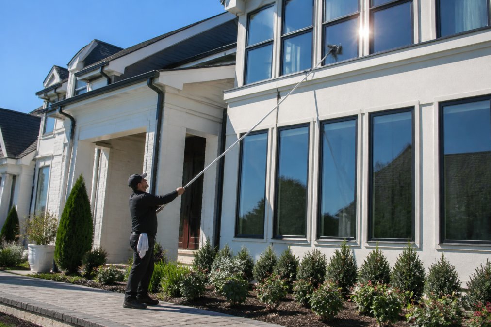 Sparkling clean residential home exterior with crystal-clear windows reflecting bright sunlight, showcasing improved curb appeal and fresh property appearance with manicured landscaping
