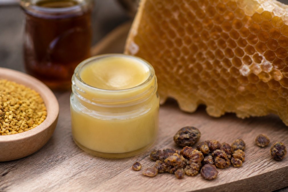 Detailaufnahme einer handwerklich hergestellten Propolis-Balsam-Flasche mit natürlichen Inhaltsstoffen und Etikett, auf Holzoberfläche mit Bienenwabe im Hintergrund