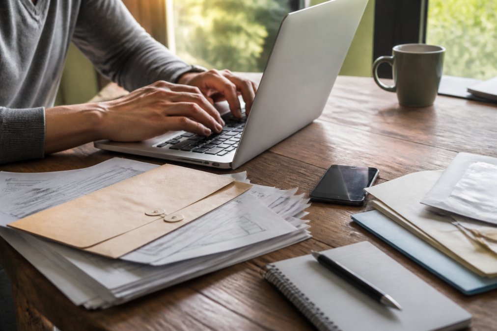Hands typing on a laptop keyboard with a smartphone and scattered documents visible on a desk, representing digital document management and cloud-based backup systems