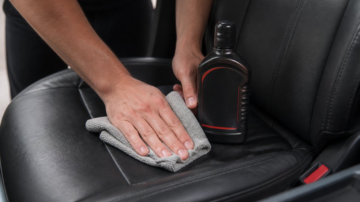 Hands gently wiping a leather car seat with a microfiber cloth to protect leather car seats during cleaning.