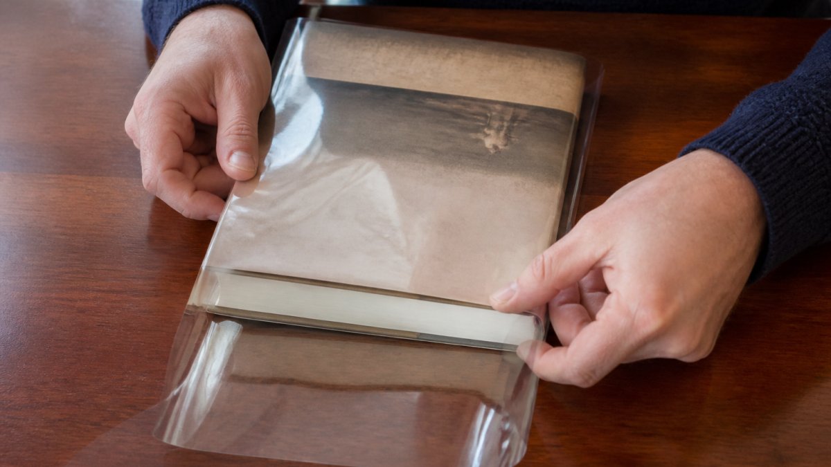 Step-by-step diagram showing hands carefully sliding a protective clear sleeve onto a hardcover book jacket