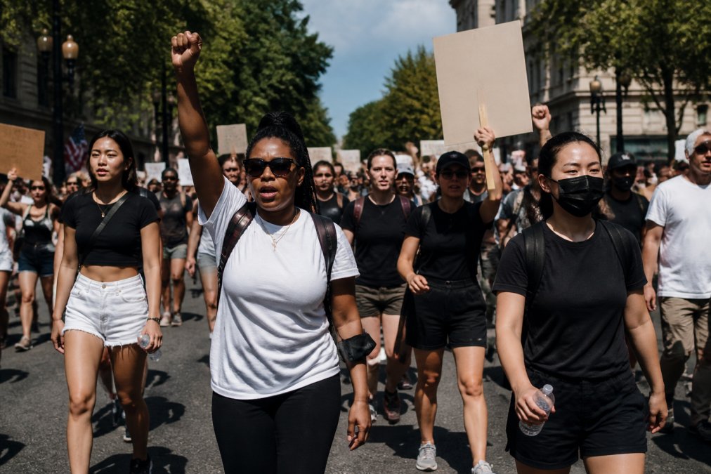 Diverse group of activists wearing statement protest tees and comfortable clothing at an outdoor march, holding signs and banners, natural daylight