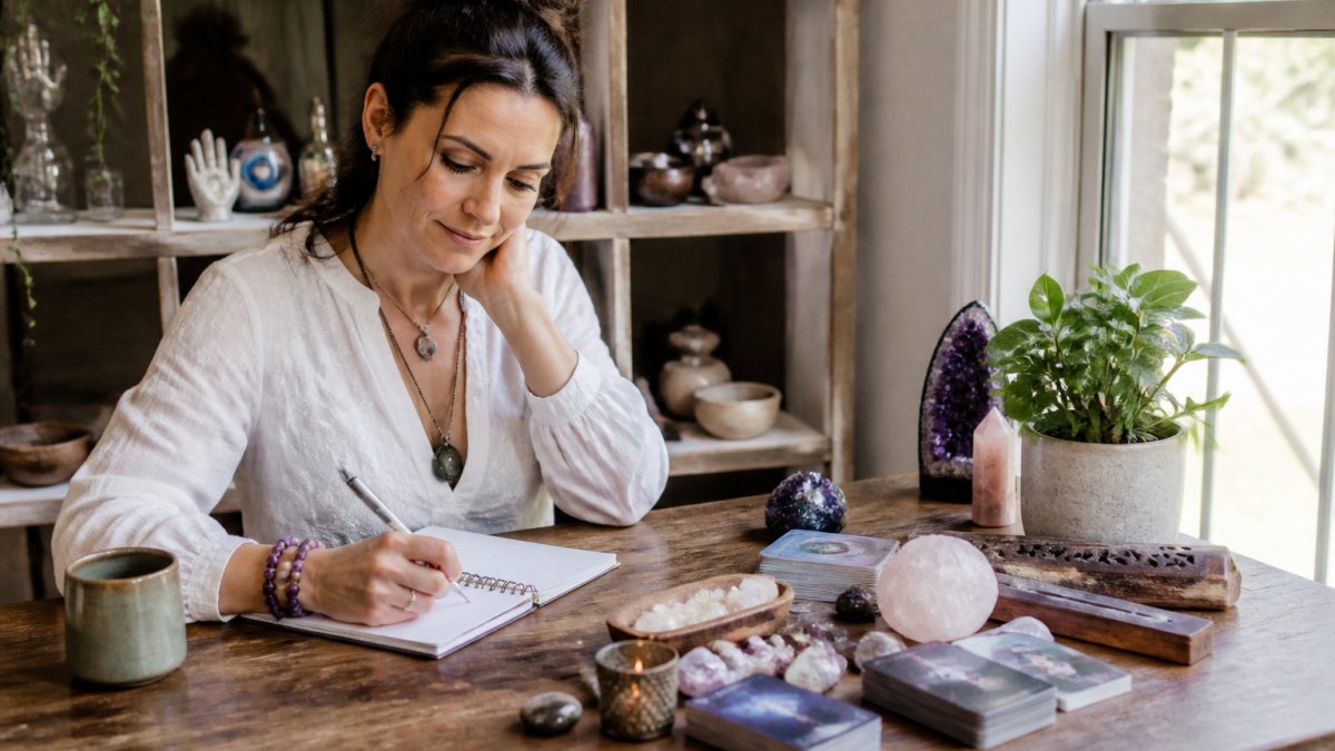 Person sitting peacefully at a wooden desk with an open journal and pen, soft natural light streaming through a window, preparing notes before a reading session
