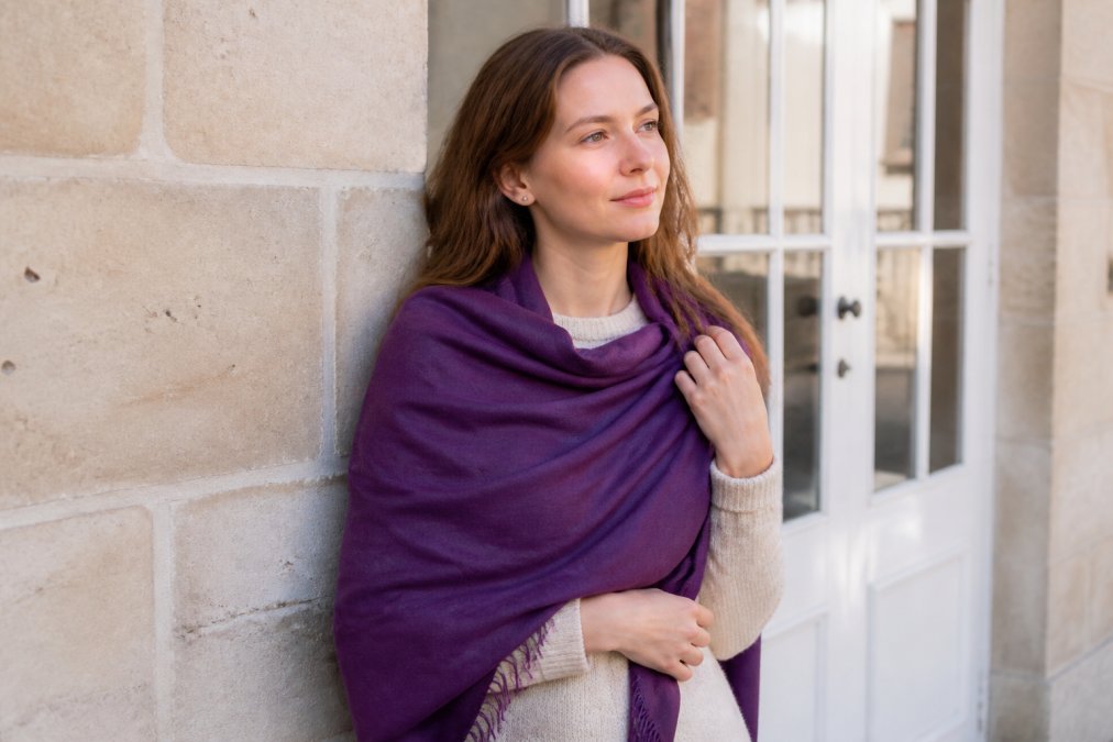 Woman wearing a rich purple pashmina shawl over a cream sweater in natural daylight