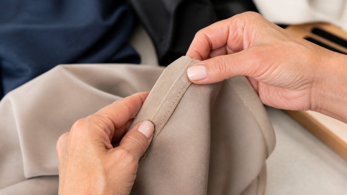 Close-up of hands carefully examining fine stitching detail on a quality garment seam, showing precise needle work and thread tension on premium fabric