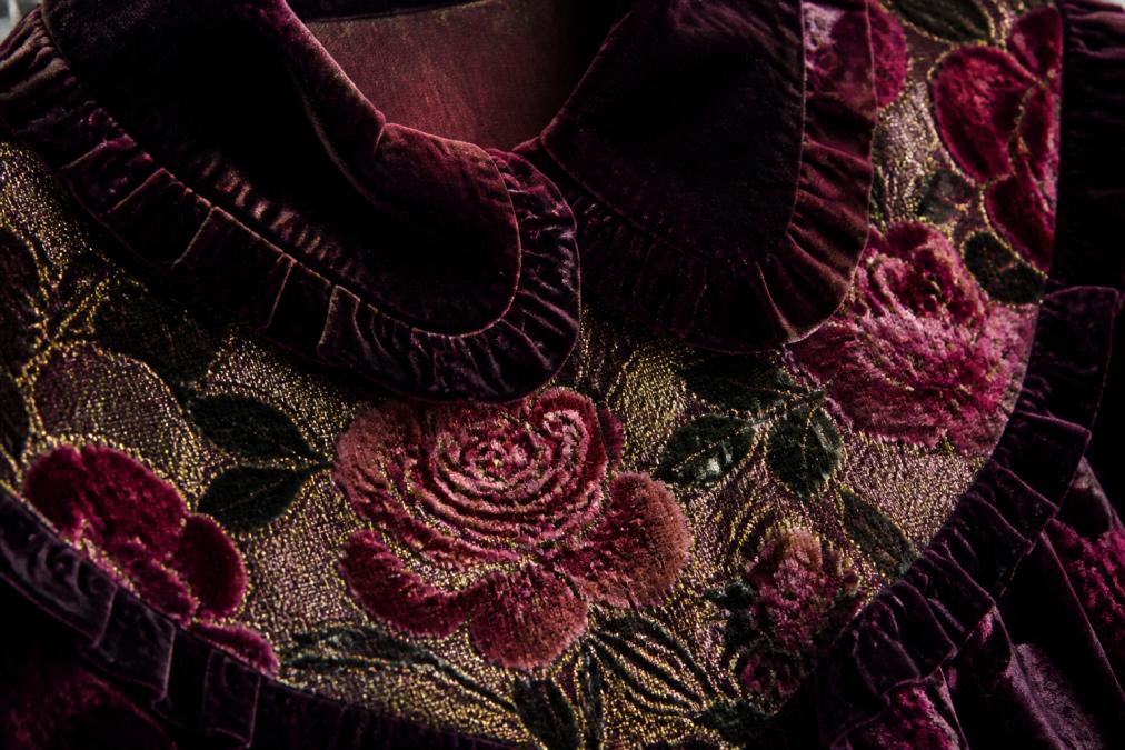 Close-up of luxurious velvet and brocade fabric textures showing intricate rose patterns and rich jewel tones, with detailed view of velvet collar and frill construction