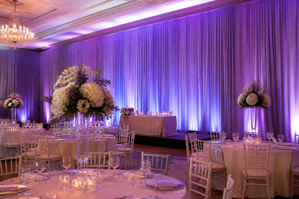 Finished upscale event space with floor-to-ceiling custom-colored draping creating dramatic backdrop, professional staging with accent lighting highlighting the fabric texture, elegant venue transformation visible with polished aesthetic