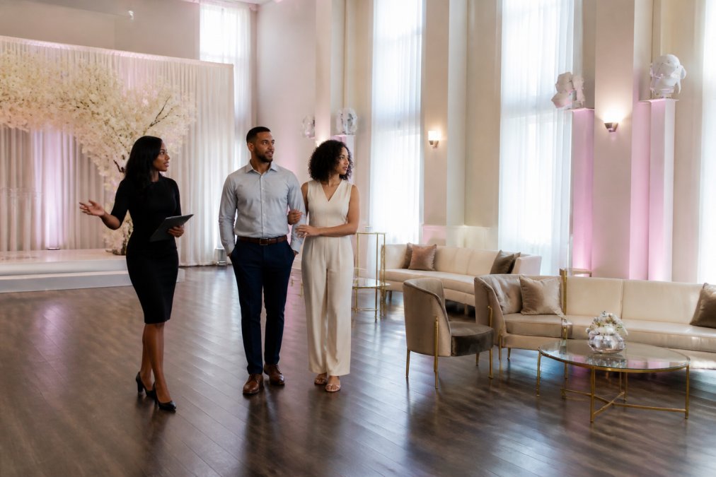 Couple reviewing ceremony space with a manager while discussing questions to ask wedding venue during a tour.