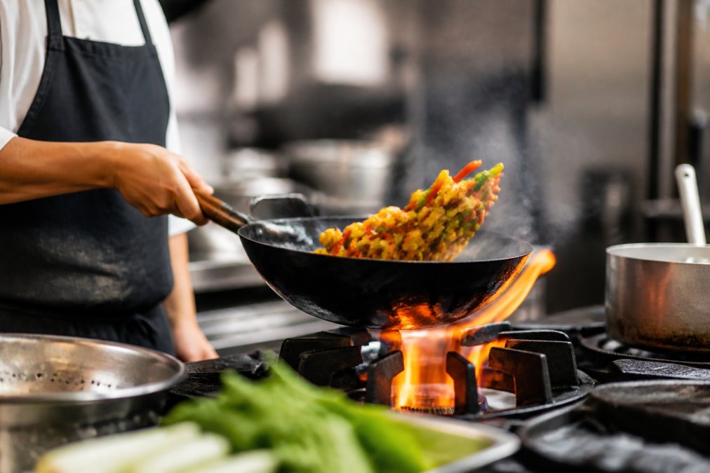 Chef tossing colorful vegetables and protein in a flaming wok to cook gluten-free stir fries.