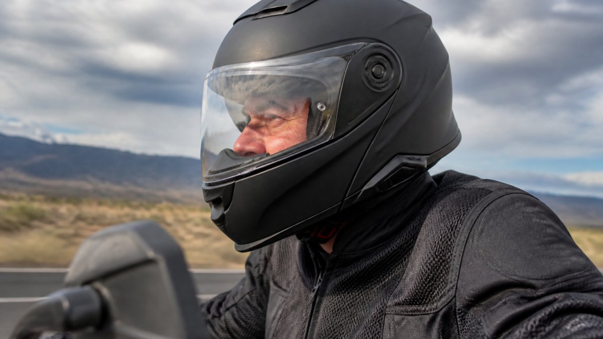 Close-up of a rider wearing a properly fitted full-face helmet on a motorcycle, showing correct positioning and seal around the face and neck area with wind flowing past