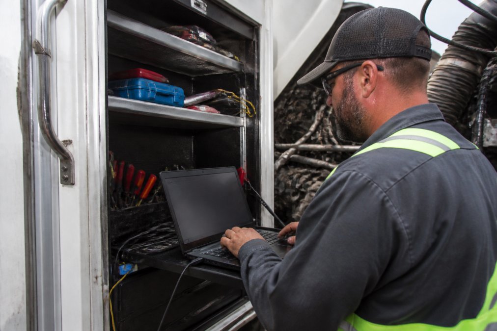 Close-up of a technician using computer diagnostic equipment inside a service truck, laptop screen displaying live engine data and fault codes, professional workspace with organized tools