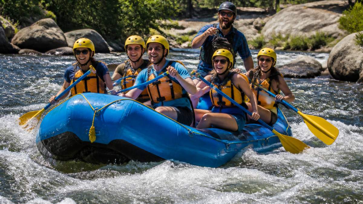 Beginners smiling while rafting vs kayaking during a guided river trip through gentle Class II rapids.