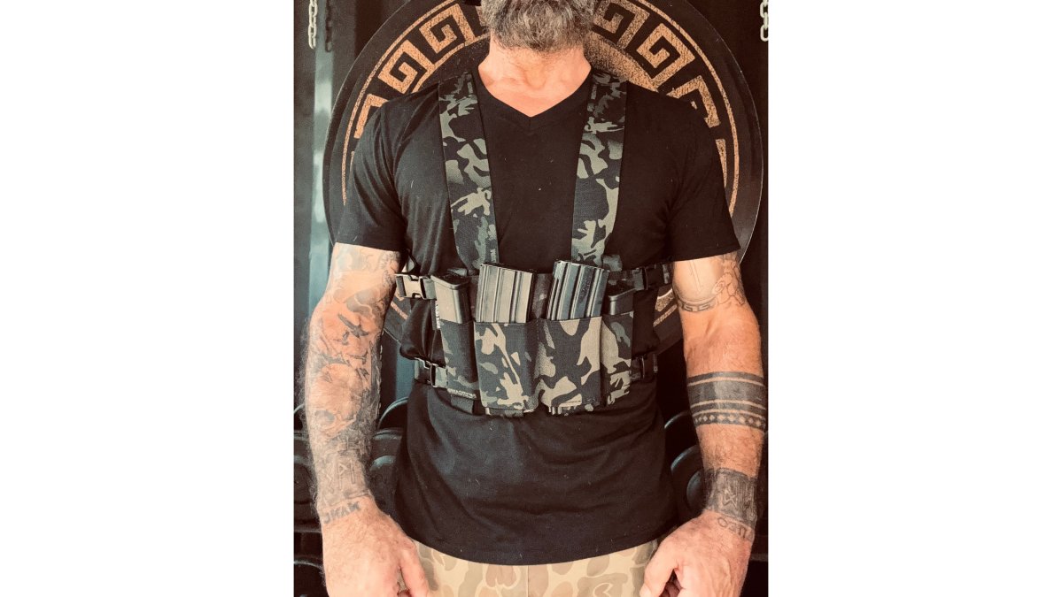 Close-up photo of a person wearing the Raider Slick Chest Rig in Black Multicam under an open light jacket, showing its low-profile fit and magazine pouches