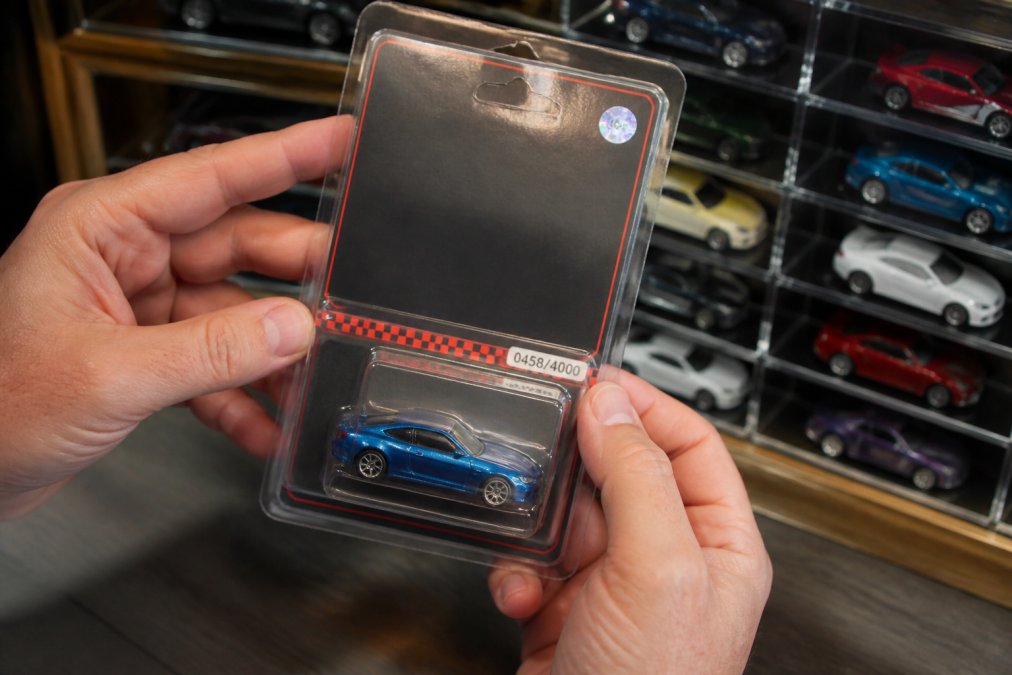 Collector holding a numbered limited edition diecast car in a blister pack with blurred display cases behind