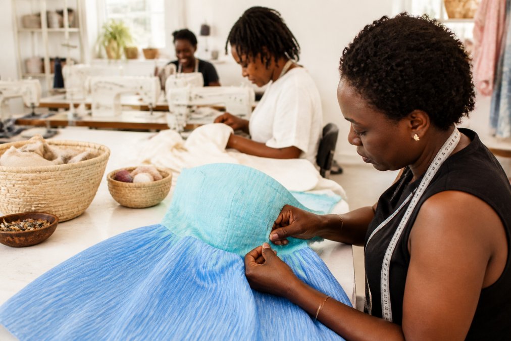 Female artisans handcrafting textiles in a bright workshop setting, showing close-up detail of hands working with traditional textile techniques and natural materials with warm natural lighting