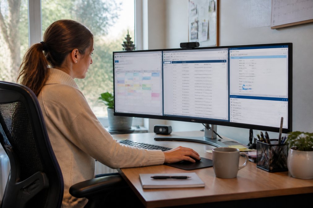 Office manager using CRM software on computer monitor with multiple windows open showing calendar, client database, and transaction tracking dashboard, afternoon natural lighting