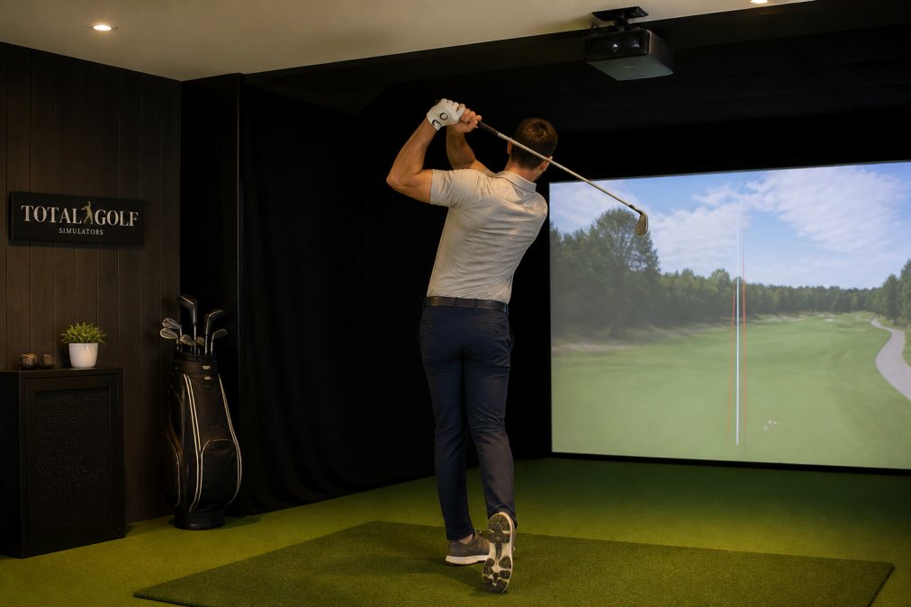 Golfer mid-swing in a home simulator bay with a ceiling-mounted launch monitor for realistic ball flight