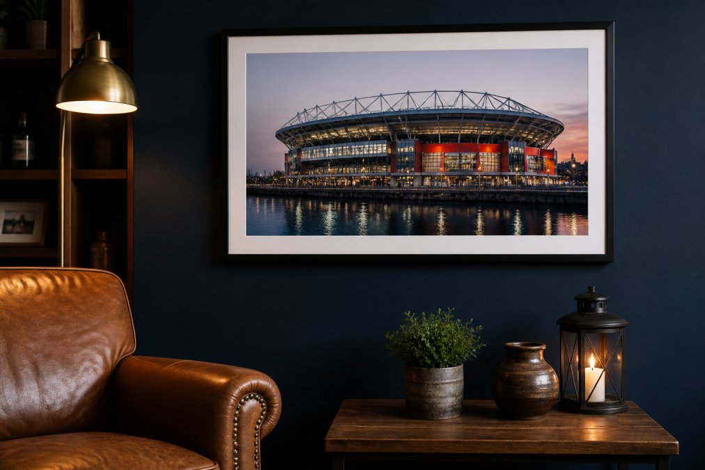 Framed photograph of a waterfront stadium displayed on a navy wall above a leather armchair and wooden table