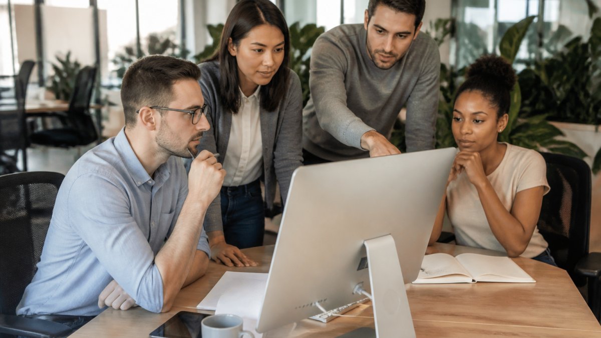 Sales manager reviewing lead data and cycle metrics on computer screen with team members gathered around discussing pipeline in modern office setting with natural lighting