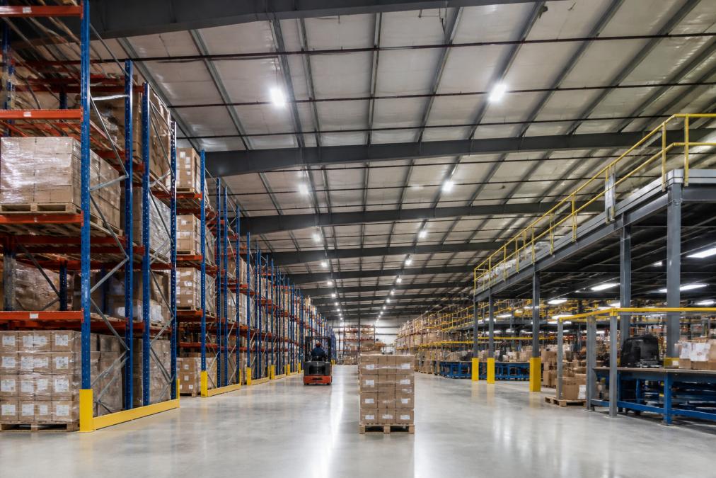 Modern LED high-bay lighting illuminating a warehouse, reducing industrial energy costs for the facility.