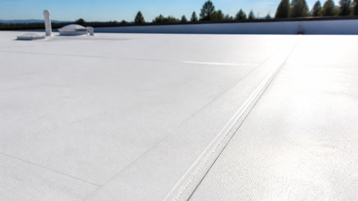 Close-up of white TPO roofing membrane surface on a flat commercial roof showing reflective white material and heat-welded seams with sunlight reflecting off the surface