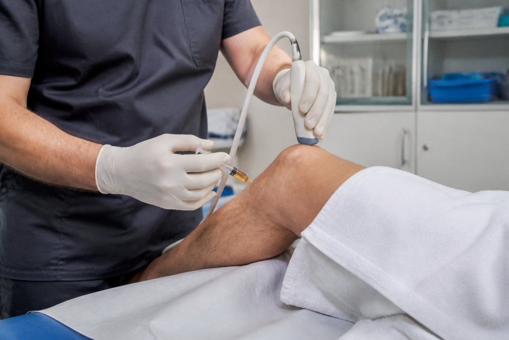 Medical professional performing ultrasound-guided PRP injection into patient's knee joint in clinical setting with sterile equipment visible