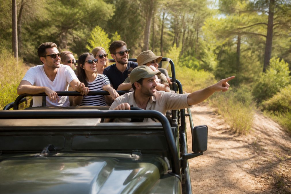 Açık jeep içinde gülümseyen turist grubu, orman ortamında, rehber eşliğinde safari esnası, güneşli hava