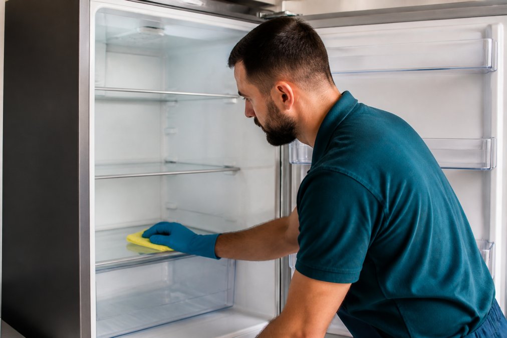 Close-up of hands cleaning the interior of a refrigerator with a cloth, demonstrating routine maintenance care in natural kitchen lighting