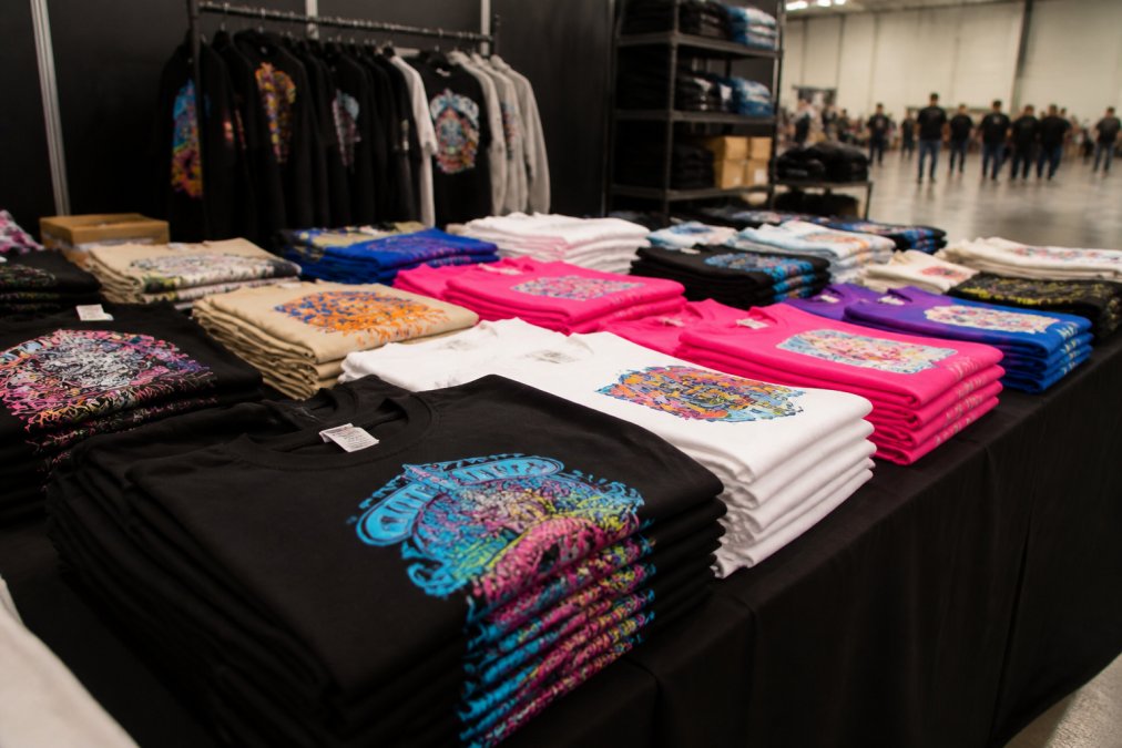 Event merchandise display featuring stacks of custom-printed t-shirts and apparel with vibrant DTF transfers in multiple colours, neatly arranged and ready for distribution at an event venue