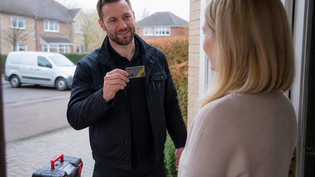 A heating engineer in workwear showing a Gas Safe ID card to a homeowner at the front door of a house, with a toolbox visible