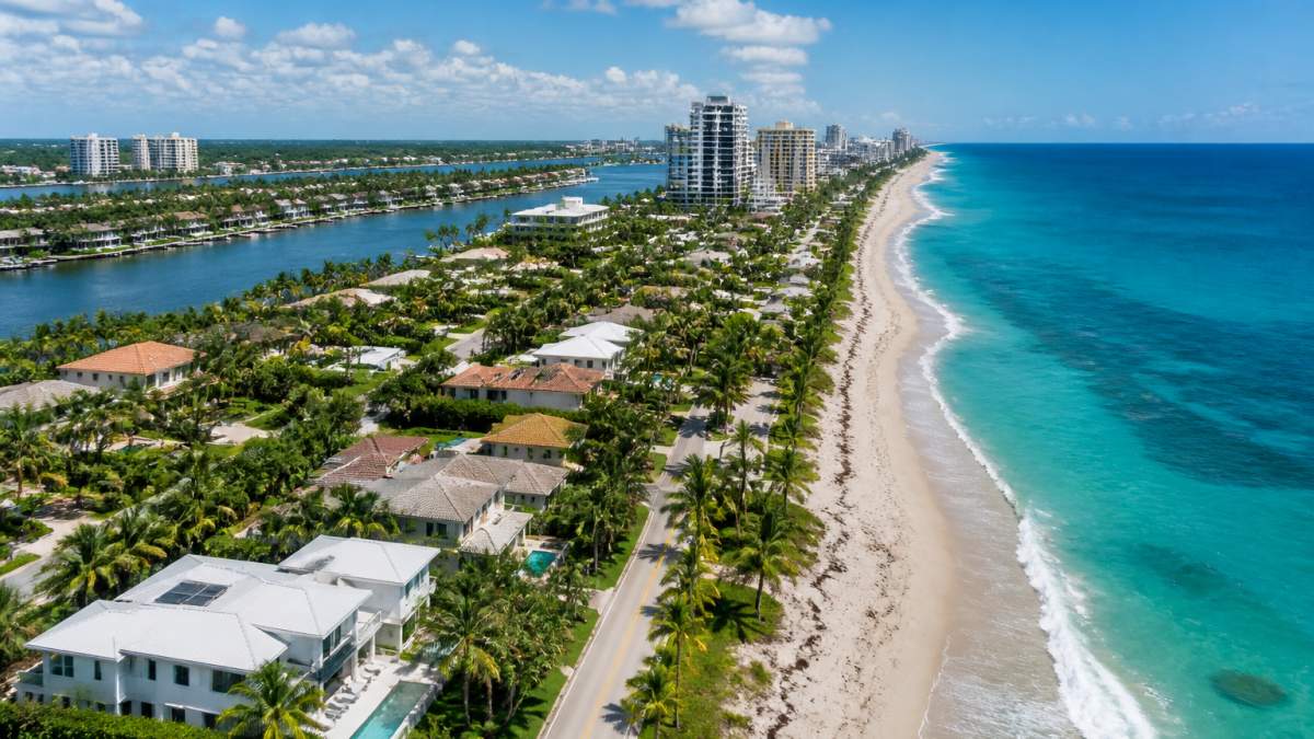 Aerial view of Palm Beach County waterfront with modern residential buildings, palm trees, and turquoise ocean waters under clear blue sky