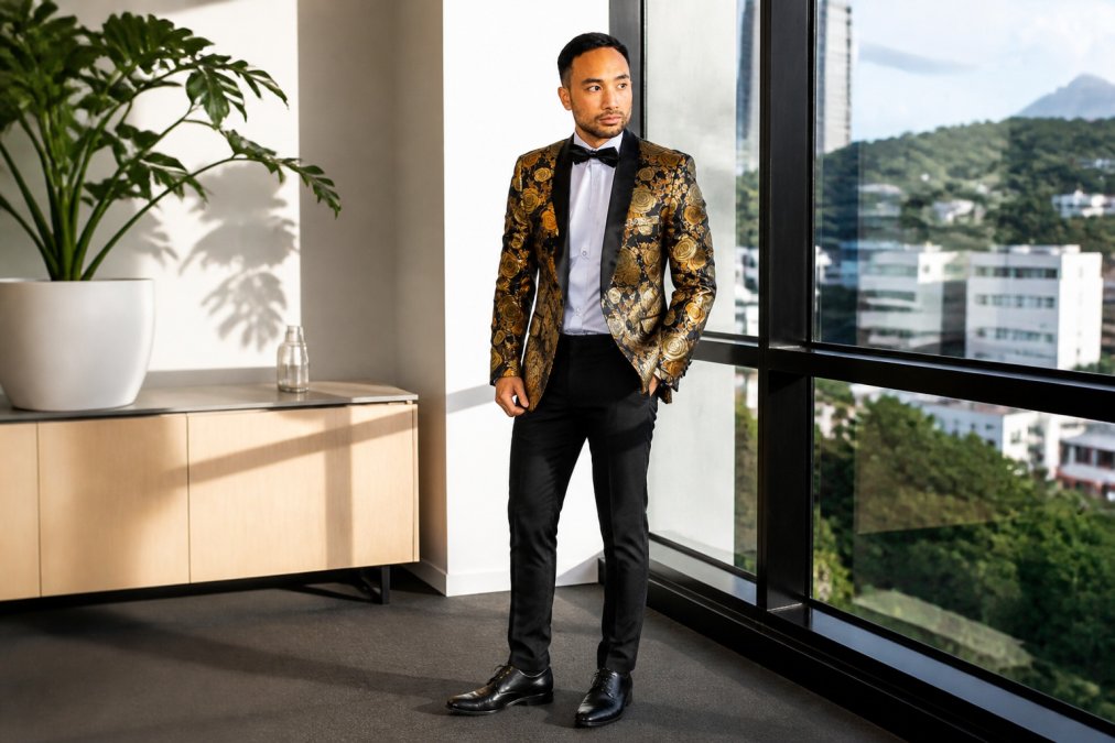 Man wearing tailored paisley jacquard blazer in gold tones with dress trousers and dress shoes, standing in modern office environment with natural window lighting