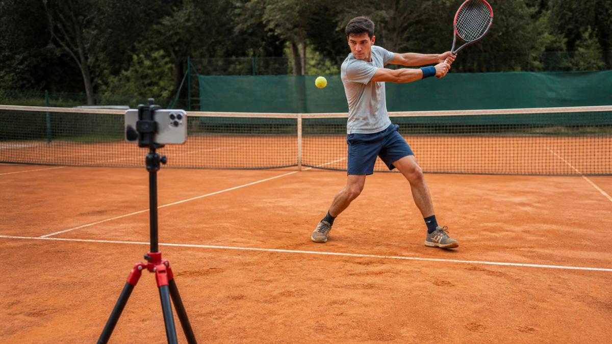 Competitive tennis player using a tripod for remote tennis stroke analysis on an outdoor clay court