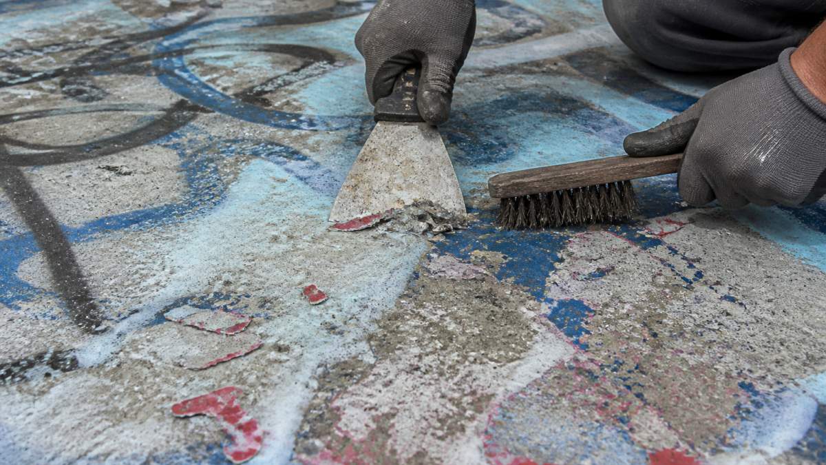 Worker using a putty knife and wire brush to remove spray paint concrete with a chemical stripper solution